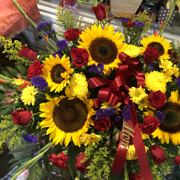Large bouquet of sunflowers, red roses, and yellow flowers with a red ribbon
