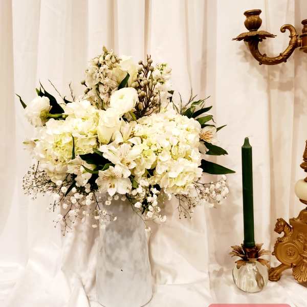 White floral arrangement in a tall vase beside a green candle