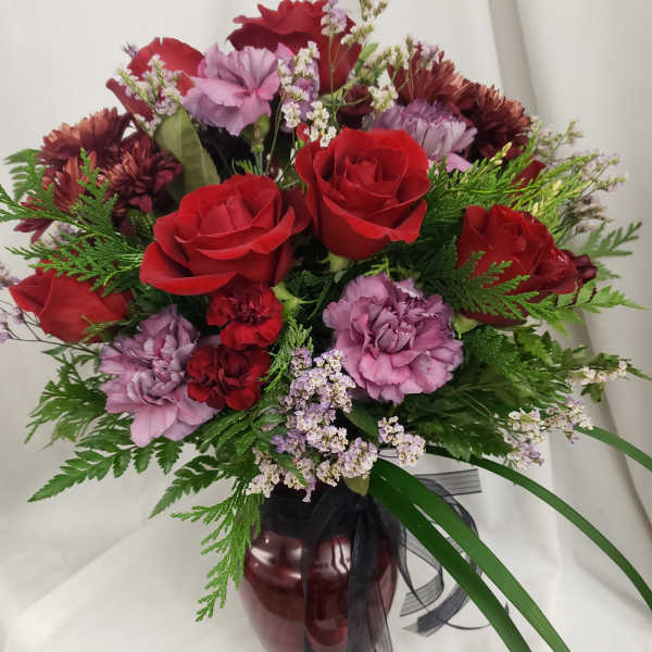 Bouquet of red roses and purple carnations in a burgundy vase