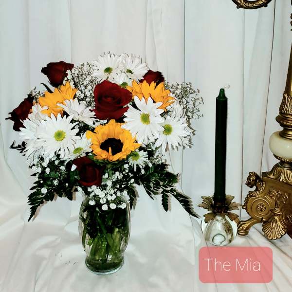 Bouquet of red roses, white daisies, and yellow sunflowers in a glass vase