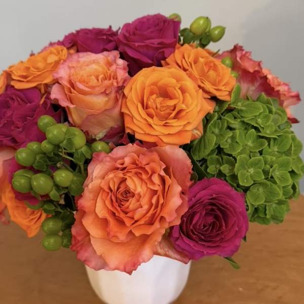 Bouquet of orange, pink, and magenta roses in a white vase