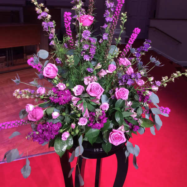 Tall floral arrangement with pink roses and purple flowers in a black stand