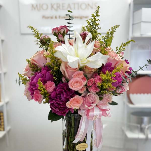 Pink and white flower bouquet in a tall glass vase with ribbon