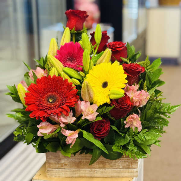 Mixed bouquet with red roses, gerbera daisies, lilies, and pink flowers in a wooden box