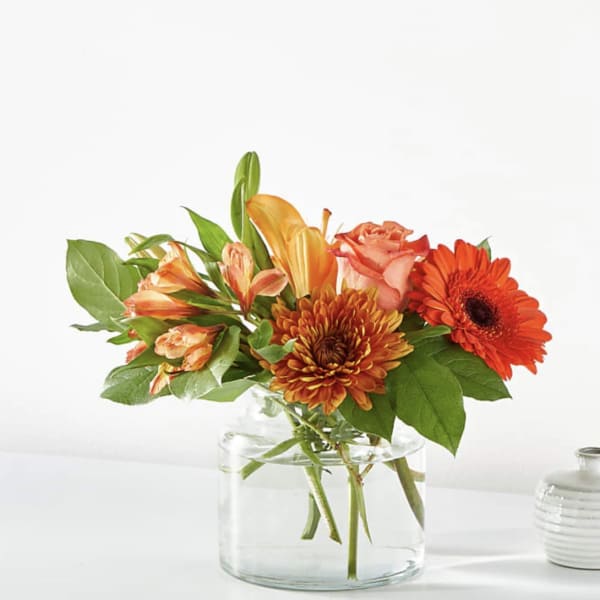 Orange and peach flowers arranged in a clear glass vase