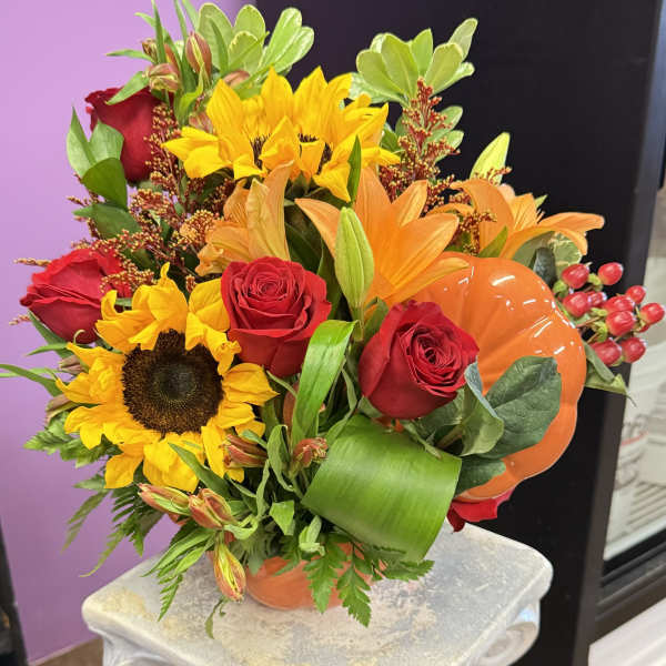 Bouquet of sunflowers, red roses, and orange lilies in a pumpkin vase