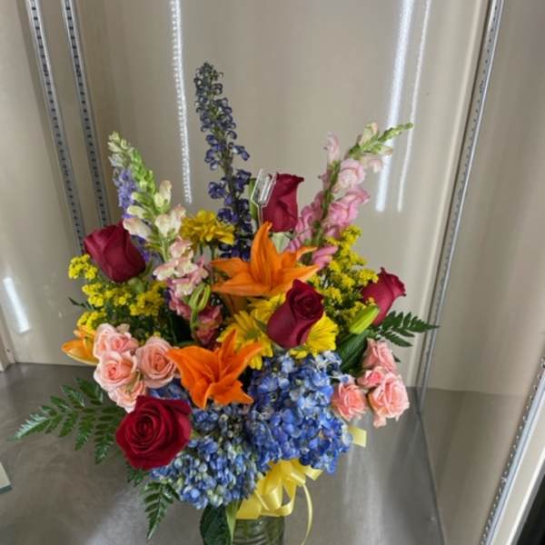 Mixed bouquet in a glass vase with roses, lilies, and blue hydrangeas