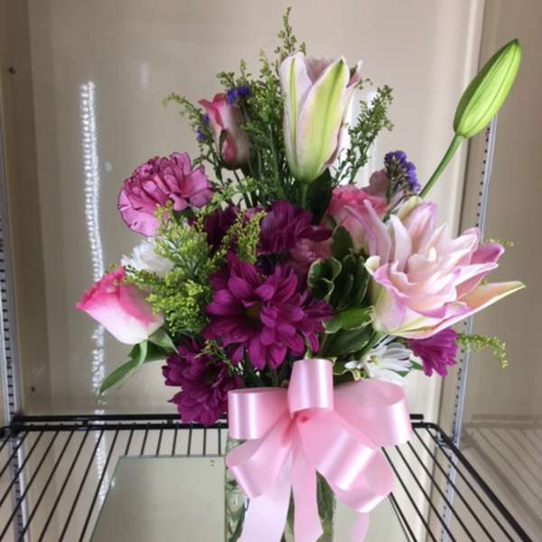 Pink and purple flower arrangement in a glass vase with a pink ribbon