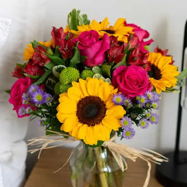 Bouquet of sunflowers, pink roses, and purple daisies in a glass vase