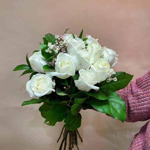 Bouquet of white roses with green foliage and small pink filler flowers