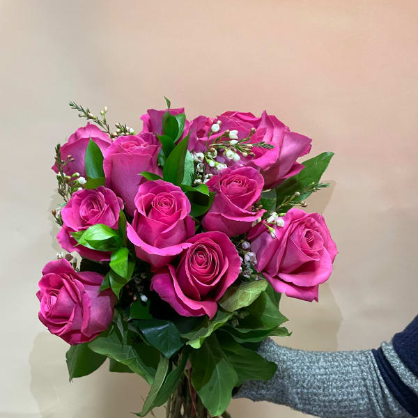Handheld bouquet of bright pink roses with small white filler flowers