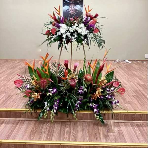 Large tropical floral tribute with white and purple flowers on a stand