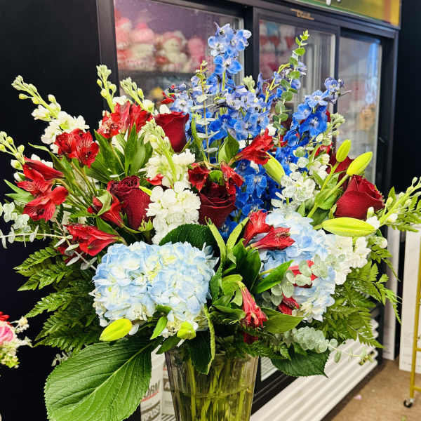 Mixed bouquet of red roses, blue delphinium, and pale hydrangeas in a glass vase