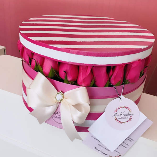 Pink roses arranged in a striped round gift box with a white bow