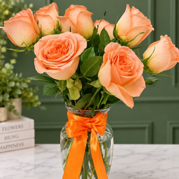 Peach roses in a clear glass vase with an orange ribbon