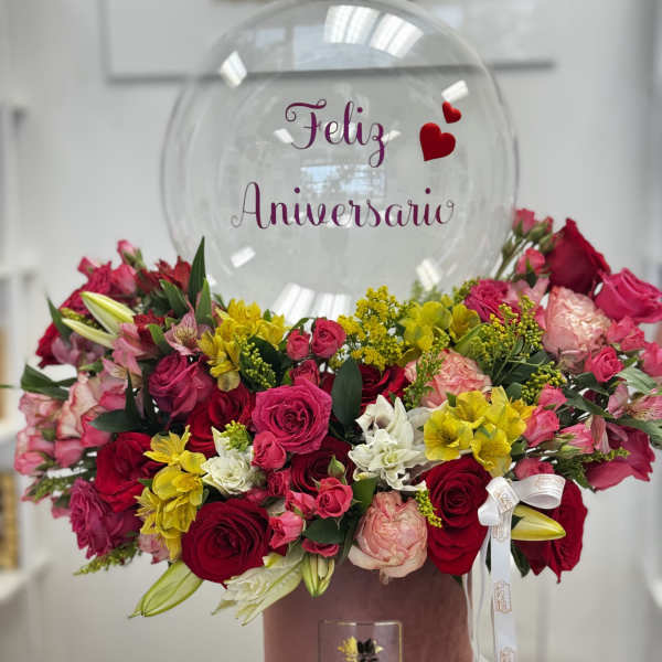 Mixed pink, red, yellow, and white flowers in a pink box with a clear anniversary balloon.