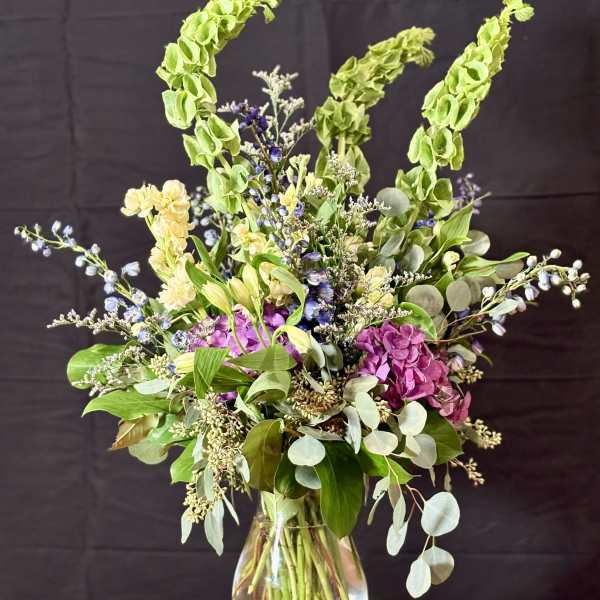 Tall mixed bouquet in a clear glass vase with purple, cream, and green blooms