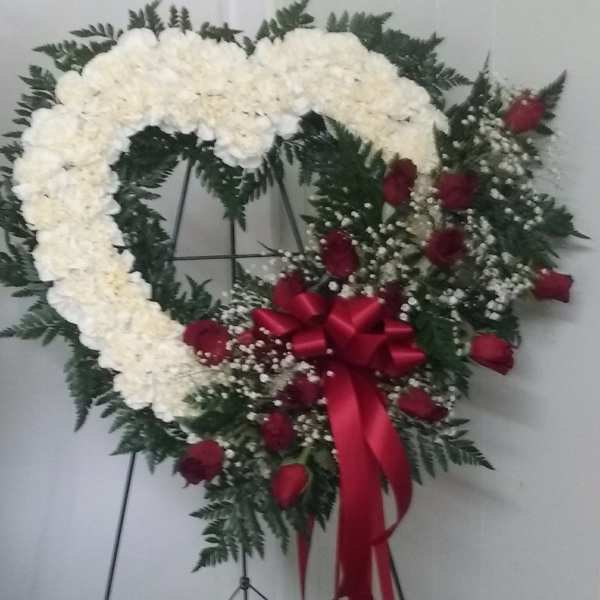 Heart-shaped white floral wreath with red roses and a red ribbon