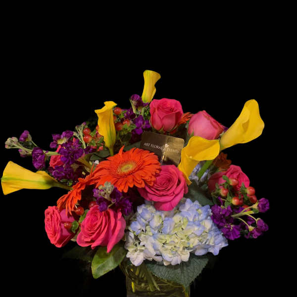Colorful bouquet with pink roses, yellow calla lilies, and blue hydrangea in a vase