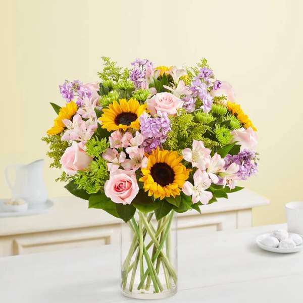 Mixed bouquet of sunflowers, pink roses, and lilac flowers in a glass vase