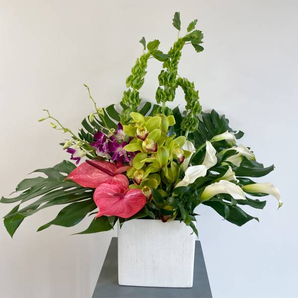 Tropical floral arrangement in a white square vase with orchids and calla lilies