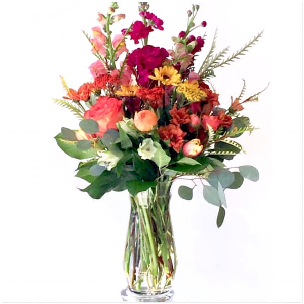 Mixed bouquet of orange, pink, and yellow flowers in a clear glass vase
