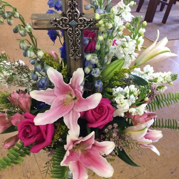 Floral arrangement with pink lilies, hot pink roses, and a wooden cross
