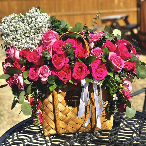 Pink roses and baby's breath in a woven basket with ribbon