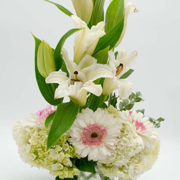 White lilies and pale flowers arranged in a clear glass vase