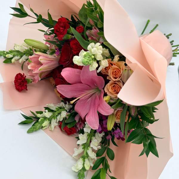 Bouquet of pink lilies, red carnations, and peach roses wrapped in blush paper