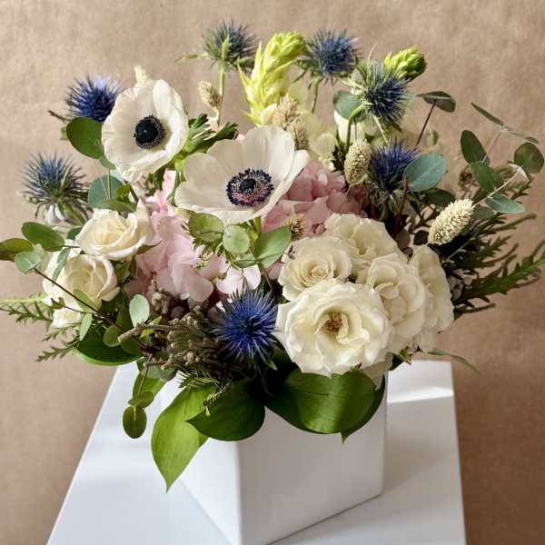 White and pink floral arrangement in a white box with blue thistle-like blooms