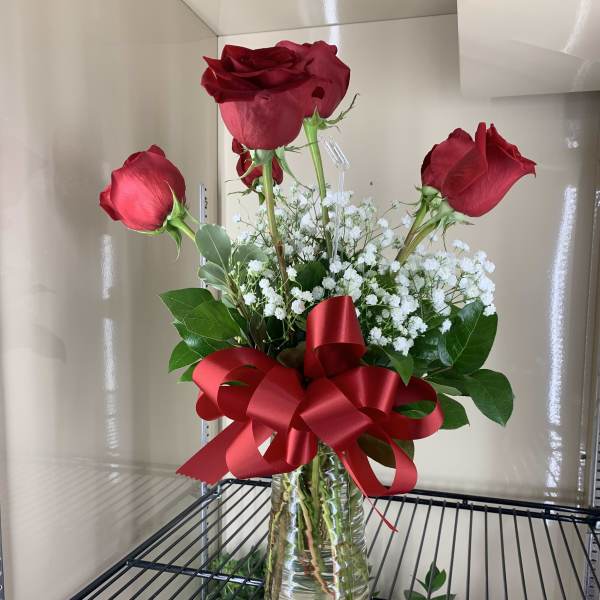 Three red roses in a glass vase with white baby's breath and a red ribbon