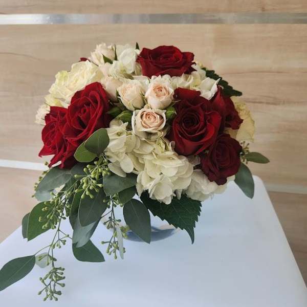 Low round arrangement of red and cream roses with hydrangeas in a clear glass bowl vase
