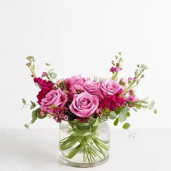 Pink roses arranged in a clear glass vase with small magenta flowers