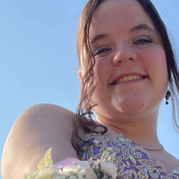 Girl wearing a purple dress holds a wrist corsage with cream roses and purple flowers