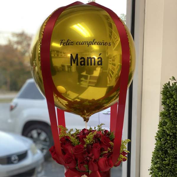 Gold balloon above red roses in a black box with a red bow