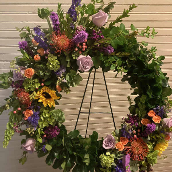 Large floral wreath on a black stand with purple, orange, and yellow blooms