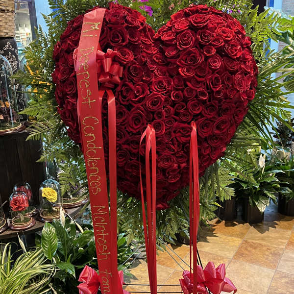 Heart-shaped red rose standing spray with red ribbons on a stand