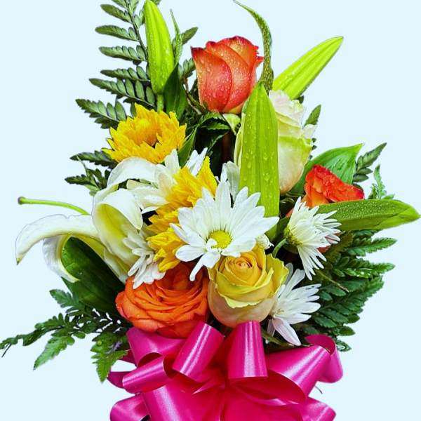 Mixed bouquet of roses, lilies, and daisies in a glass vase with a pink ribbon