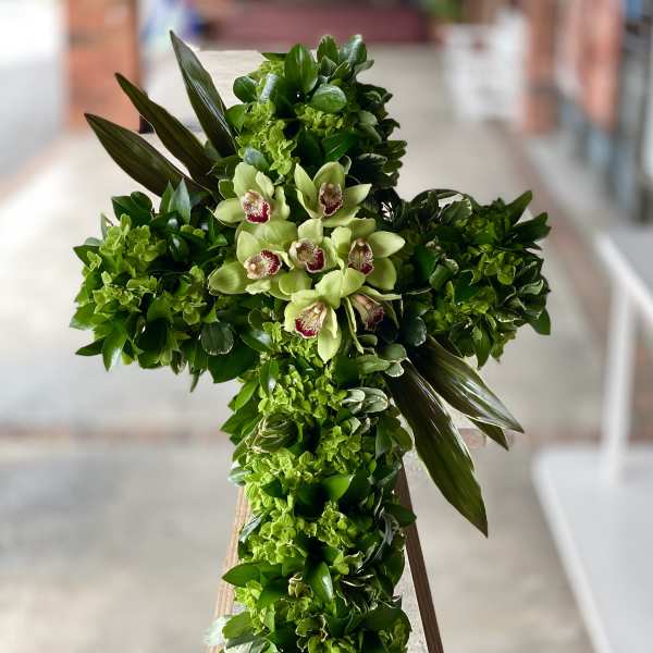 Green floral cross with pale orchids on a stand