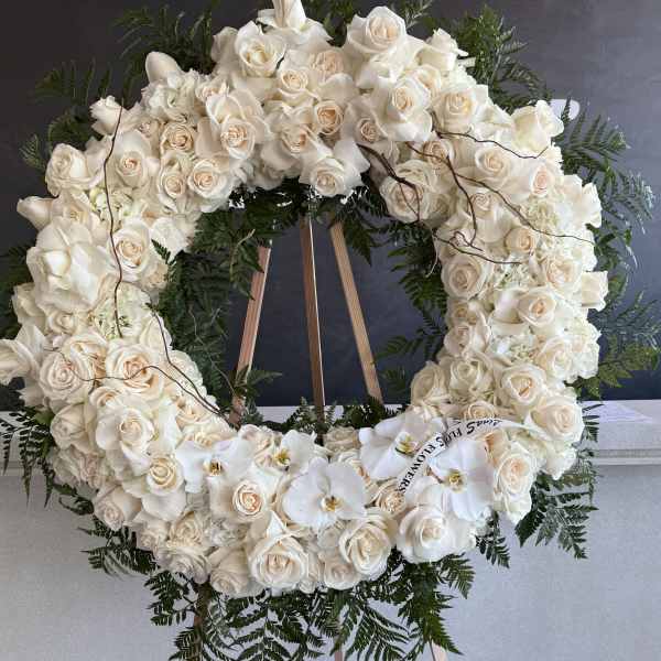 Large white rose wreath on a wooden easel with orchids and greenery