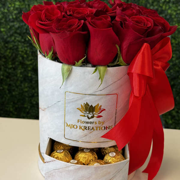 Red roses in a white gift box with gold chocolates and a red ribbon