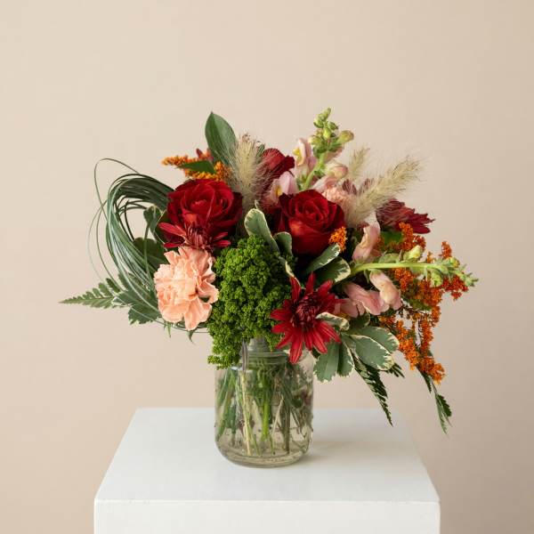 Mixed bouquet of red, pink, and orange flowers in a glass jar vase