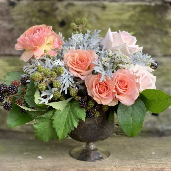 Peach roses and pink blooms in a metal pedestal vase