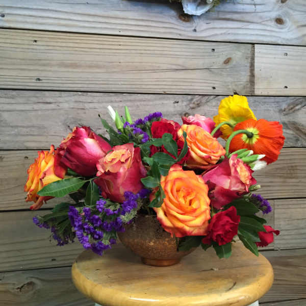 Bouquet of multicolored roses with purple filler in a copper vase