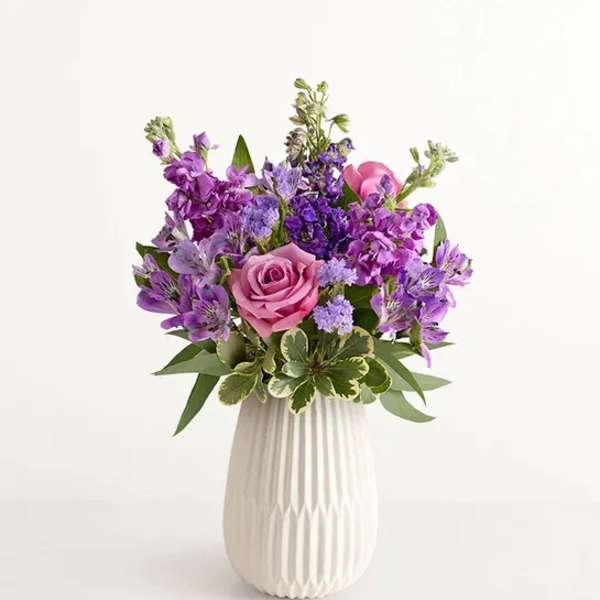 Purple and pink flower arrangement in a white vase