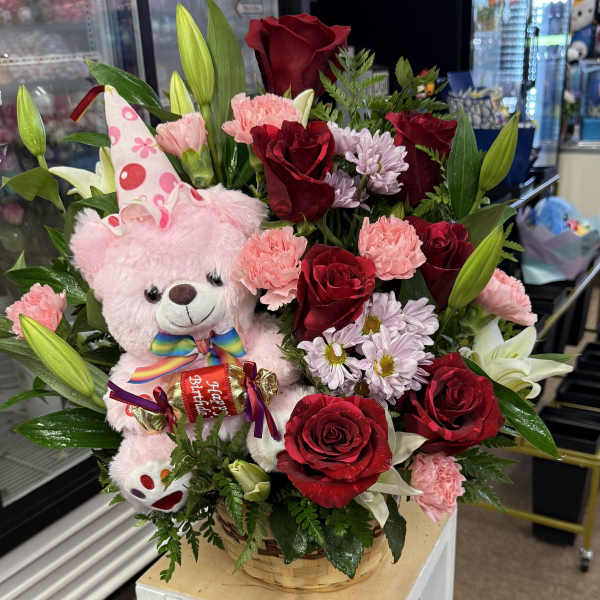 Basket arrangement with red roses, pink carnations, lilies, and a pink teddy bear