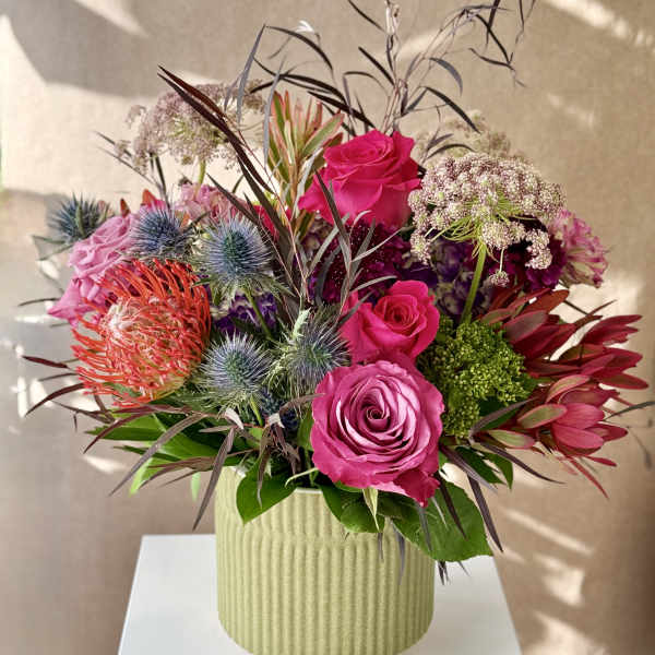 Bouquet of pink roses and spiky flowers in a ribbed green vase