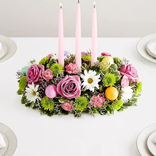 Pink floral centerpiece with three tall candles on a table