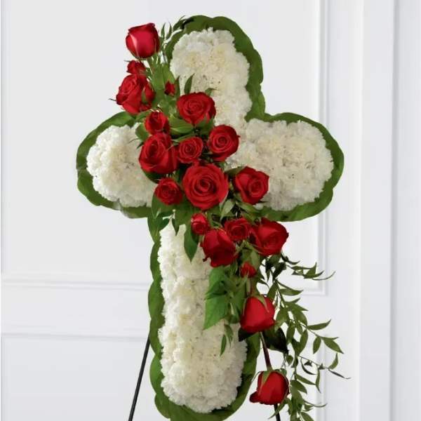 Cross-shaped floral tribute with red roses and white flowers on an easel